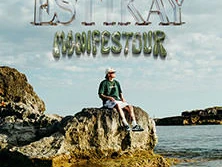 Ein Musiker sitzt auf einem Felsen am Wasser unter einem bewölkten Himmel mit der Aufschrift "ESTIKAY MANIFESTOUR".