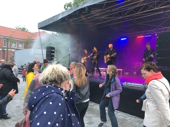 Feierabend Konzert in Pewsum: Before Sunset Eine Live-Band spielt auf einer Open-Air-Bühne, davor tanzen Menschen ausgelassen.