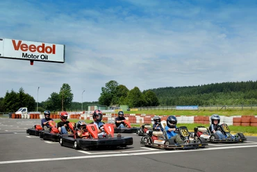 Kartbahn Mehrere Personen fahren in roten und schwarzen Karts auf einer Rennstrecke im Freien.