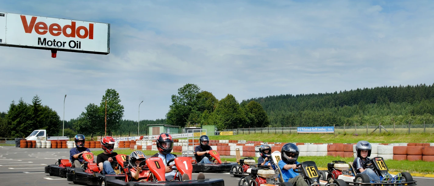 Kartbahn Mehrere Personen fahren in roten und schwarzen Karts auf einer Rennstrecke im Freien.