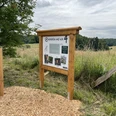 Hexenpfad Dorf Olpe Informationstafel einer Wanderroute in ländlicher Landschaft mit Feldern und bewölktem Himmel.