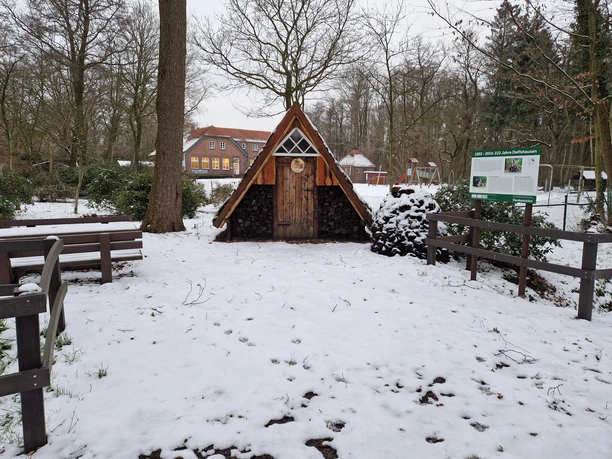 Plaggenhütte_Winter_quer.jpg Eine kleine, rustikale Hütte aus Holz mit dreieckigem Dach steht im verschneiten Wald.