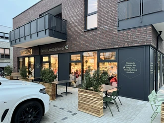 Moderne Bäckerei mit Außensitzplätzen, großen Fenstern und einladend beleuchtetem Innenraum