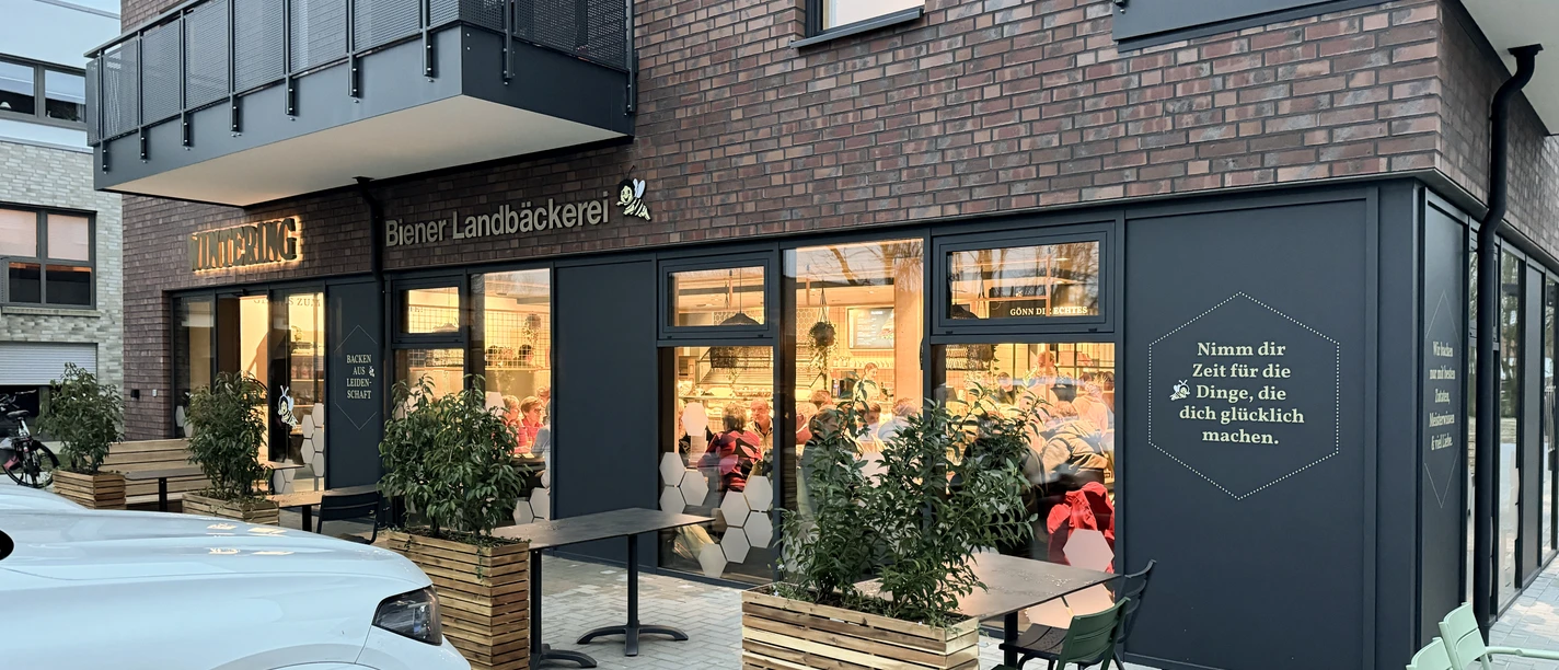 Moderne Bäckerei mit Außensitzplätzen, großen Fenstern und einladend beleuchtetem Innenraum