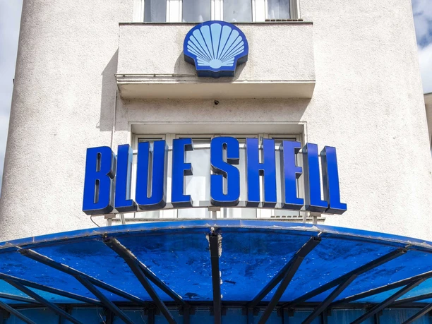Blue Shell Das Bild zeigt den Eingangsbereich des Veranstaltungsortes „Blue Shell“ in Köln. Über dem Eingang prangt ein auffälliges, blaues Schild mit dem Schriftzug „Blue Shell“. Das Gebäude hat eine helle Fassade, wobei der Eingangsbereich in Blau gehalten ist. Ein Vordach aus Metall bietet Schutz vor Witterungseinflüssen und unterstreicht das zeitgemäße Design des Clubs.