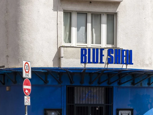 Blue Shell Die Fassade des bekannten Kölner Clubs "Blue Shell" in leuchtendem Blau mit markantem Muschel-Logo.The facade of the well-known Cologne club "Blue Shell," in vibrant blue featuring its distinctive shell logo.