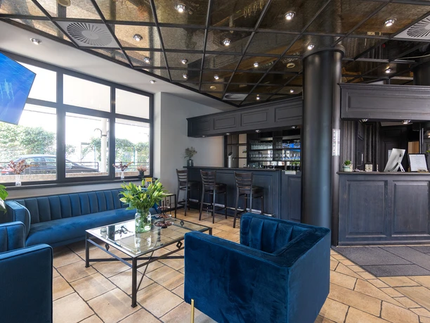 Lobby mit Bar, Rezeption und blauen Sitzmöbeln, große Fenster und Beleuchtung