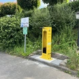 Radservice-Station Gelbe Fahrrad-Servicestation neben einem Parkplatzschild, umgeben von dichter grüner Vegetation.