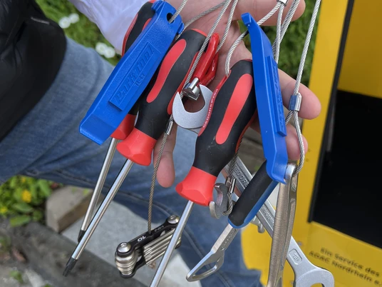 Radservice-Station Hand hält mehrere Fahrradinstandsetzungswerkzeuge, darunter Schraubenschlüssel und Schraubendreher.