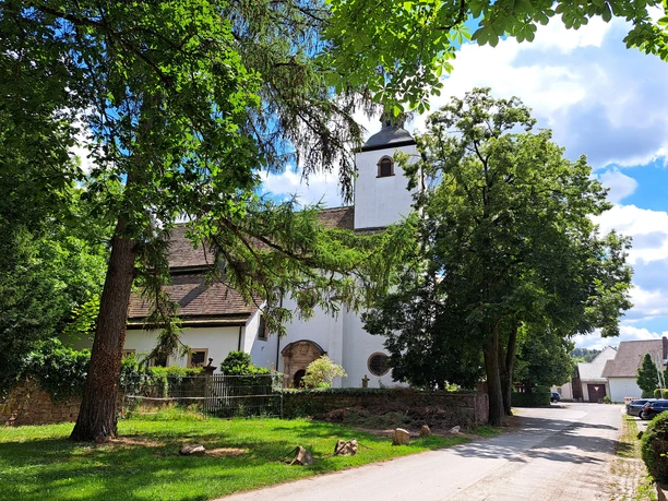 Kath. Pfarrkirche Hl. Familie und Hl. Stephanus in Wehrden Weißes Kirchengebäude mit Kirchturm, umgeben von einer alten Mauer und Bäumen