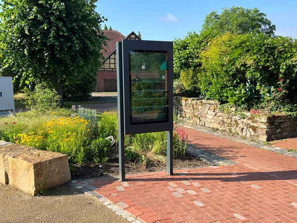 The Winzlar information terminal set against a picturesque backdrop featuring plants and a historic building in the background.