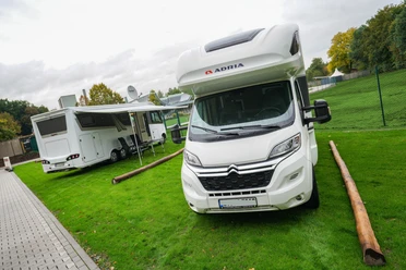 Wohnmobilstellplatz an der Welle Gütersloh Zwei Wohnmobile auf markierten Stellplätzen neben Grünfläche und Zaun am Freizeitbad.