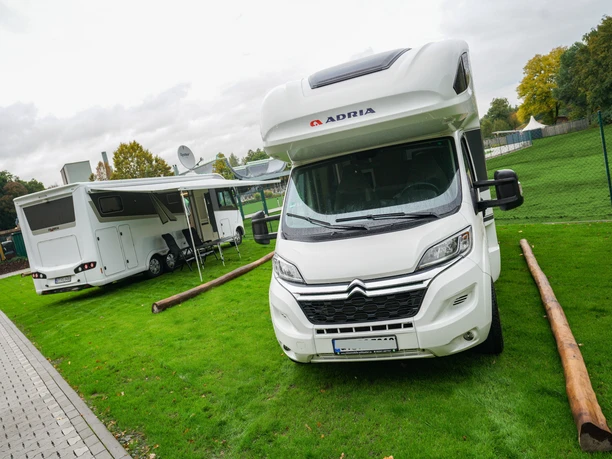 Wohnmobilstellplatz an der Welle Gütersloh Zwei Wohnmobile auf markierten Stellplätzen neben Grünfläche und Zaun am Freizeitbad.