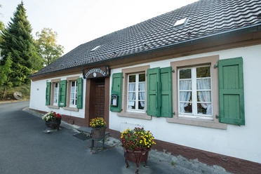 Stindermühle in Erkrath.jpg Weißes Gebäude mit grünen Fensterläden und einem Schild "Stindermühle", flankiert von Blumenkübeln.