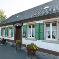 Stindermühle in Erkrath.jpg Weißes Gebäude mit grünen Fensterläden und einem Schild "Stindermühle", flankiert von Blumenkübeln.