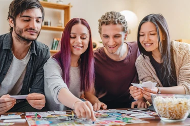 Vier junge Erwachsene spielen ein Brettspiel und lachen am Tisch.