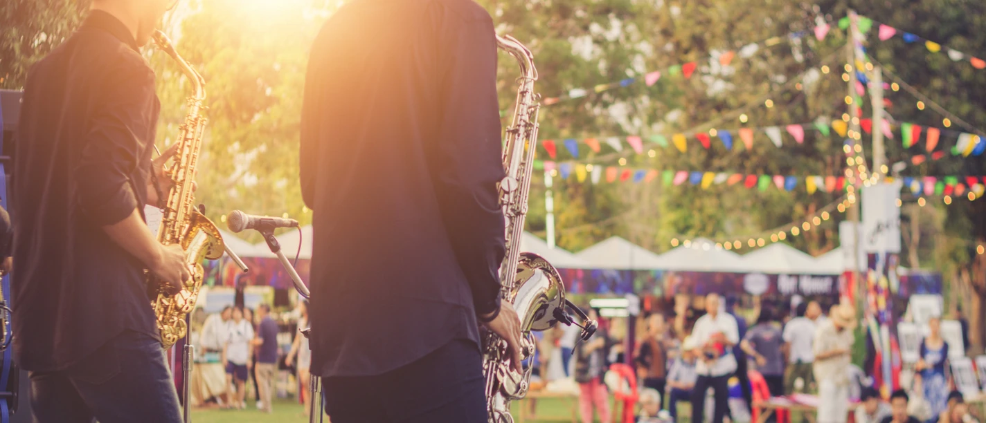 bo events Zwei Saxophonisten auf Bühne, davor Publikum auf bunt geschmückter Grünfläche.
