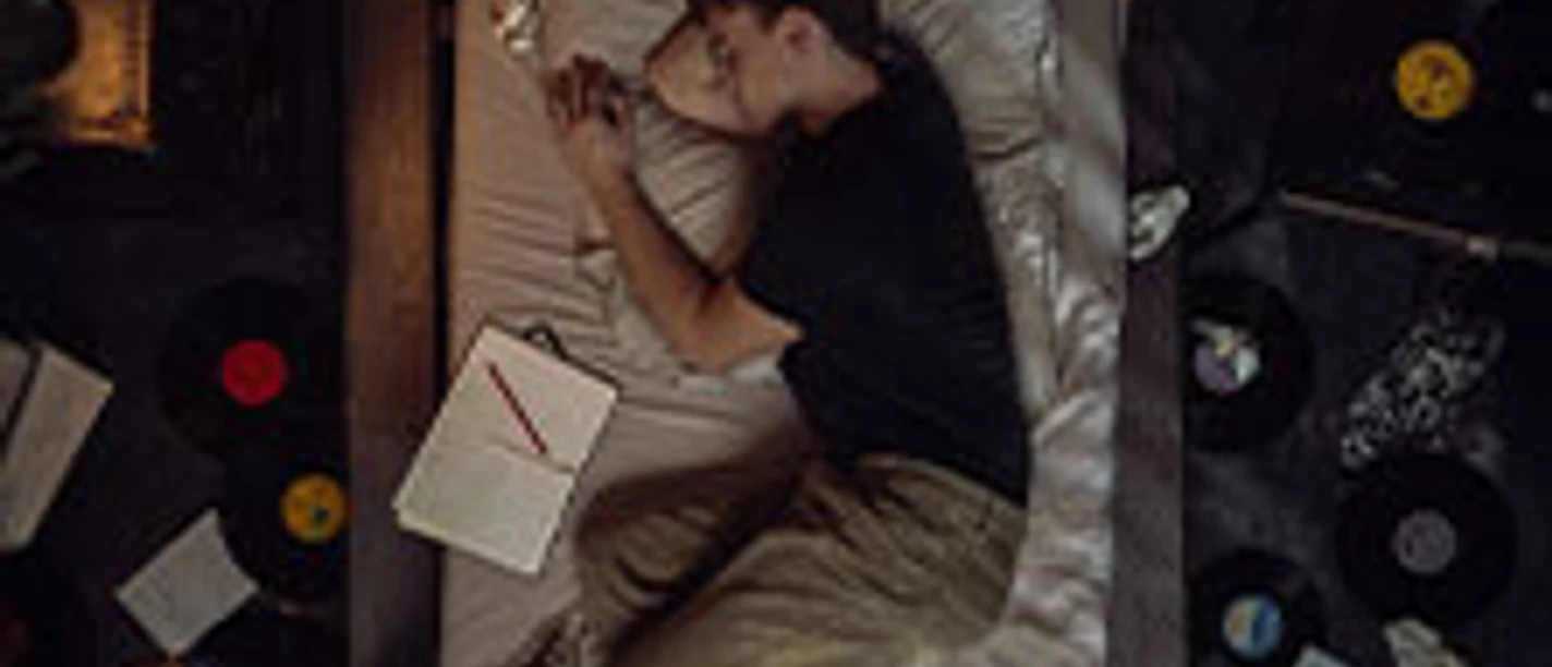 Marlon Hammer schläft gemütlich in einem Bett, umgeben von Vinyl-Schallplatten und offenen Notizbüchern.