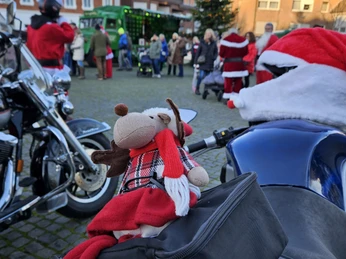 Ausschank unterm Weihnachtsbaum Weihnachtliche Marktszene mit Kuscheltier-Rentier auf einem Motorrad in festlicher Umgebung.