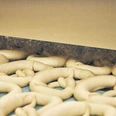 Bäckerei Aurhammer Frische Teiglinge in Form von Brezeln auf einem Förderband in einer Bäckerei.