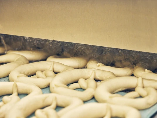 Bäckerei Aurhammer Frische Teiglinge in Form von Brezeln auf einem Förderband in einer Bäckerei.