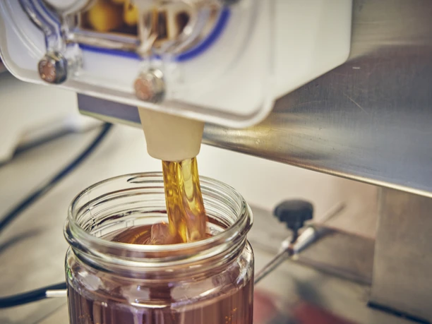 BienenFranz Honig fließt aus einem Spender in ein Glasgefäß.