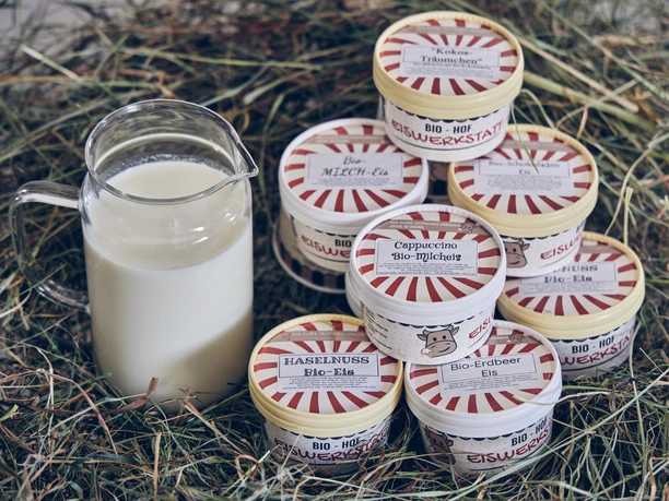 Bio-Hof-Eiswerkstatt Eine Glaskanne Milch neben Eisbechern auf Heu.