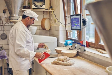 Bäckerei Brandmeier Ein Bäcker formt Teig auf einem Arbeitstisch in einer Backstube.