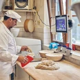 Bäckerei Brandmeier Ein Bäcker formt Teig auf einem Arbeitstisch in einer Backstube.