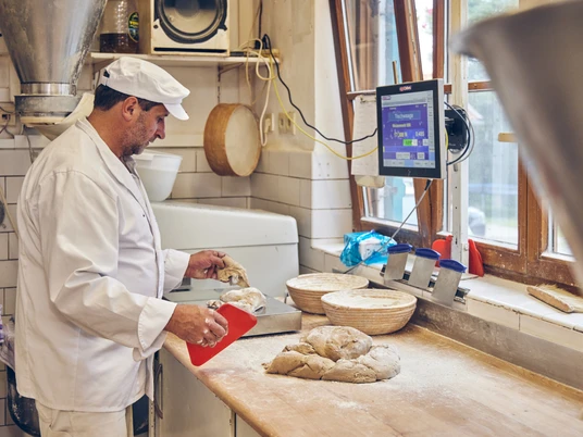 Bäckerei Brandmeier Ein Bäcker formt Teig auf einem Arbeitstisch in einer Backstube.