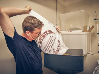 Bierbrauerei im Hotel Garmischer Hof Ein Mann füllt Malz aus einem großen Sack in einen Trichter.