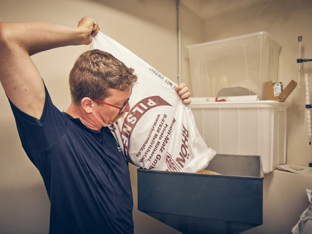Bierbrauerei im Hotel Garmischer Hof Ein Mann füllt Malz aus einem großen Sack in einen Trichter.