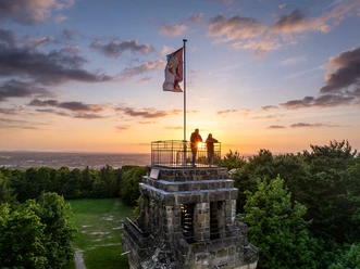 Herford-Bismarckturm-2025-075-©Teutoburger Wald - WfG Herford - D. Ketz.jpg Bismarckturm Herford in abendlicher Kulisse, zwei Menschen genießen den Sonnenuntergang auf der Plattform.