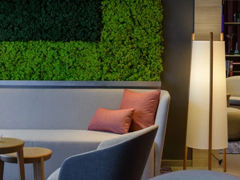 Moderne Hotellobby mit grauem Sofa, orangefarbenen Kissen und vertikaler Mooswand im Hintergrund.