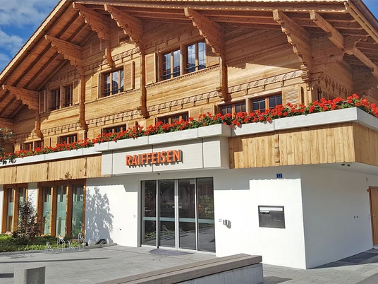 Head office of Raiffeisenbank Niedersimmental in Oey Mehrstöckiges Holzchalet mit roter Logoaufschrift RaiffeisenMulti-storey wooden chalet with red Raiffeisen logo letteringChalet en bois à plusieurs étages avec inscription rouge du logo Raiffeisen