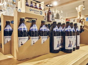 Glentleitner Wirtschaft & Brauerei Sechserträger und Kisten mit Glentleitner Bierflaschen auf einem Holzregal.