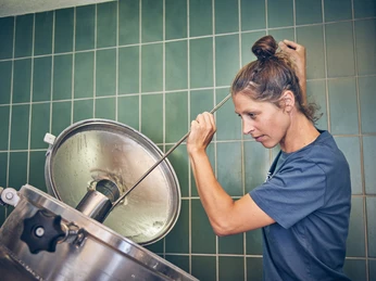 Brauerei Karg Eine Person rührt in einem Braukessel vor einer grünen Kachelwand.