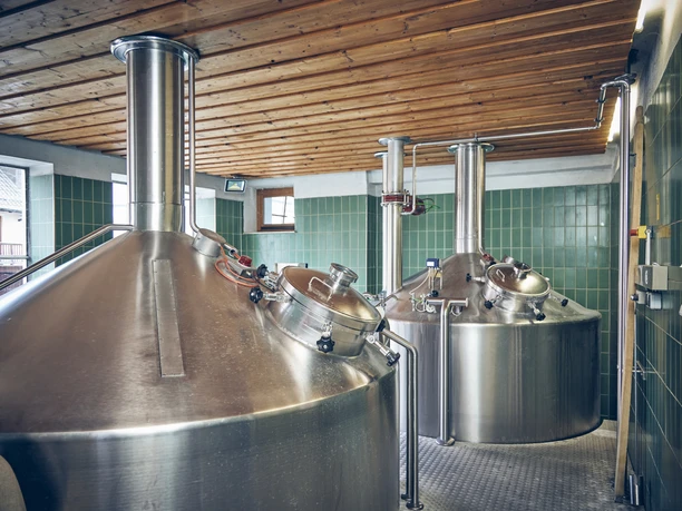 Brauerei Karg Große Edelstahl-Braukessel in einer Brauerei mit grünen Fliesen und Holzdach.