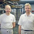 Bäckerei Josef Krätz Zwei Männer in Arbeitskleidung stehen in einer Backstube vor Öfen.
