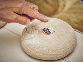 Bäckerei Josef Krätz Hand zeigt auf ein rundes, unbedeutetes Brot mit einem Aufkleber "Spitzenprodukt".