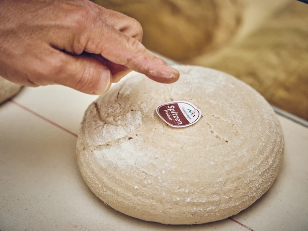Bäckerei Josef Krätz Hand zeigt auf ein rundes, unbedeutetes Brot mit einem Aufkleber "Spitzenprodukt".