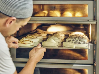 Bäckerei Josef Krätz Bäcker schiebt Bleche mit frischen Teigschnecken in einen heißen Ofen.