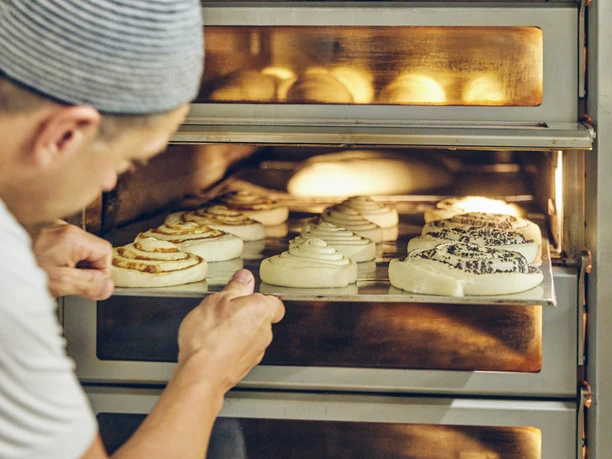 Bäckerei Josef Krätz Bäcker schiebt Bleche mit frischen Teigschnecken in einen heißen Ofen.