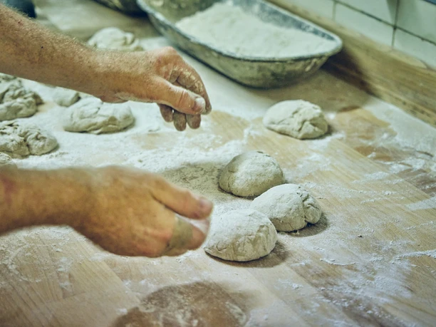 Bäckerei Josef Krätz Hände formen Teigkugeln auf einer bemehlten Arbeitsfläche in einer Bäckerei.