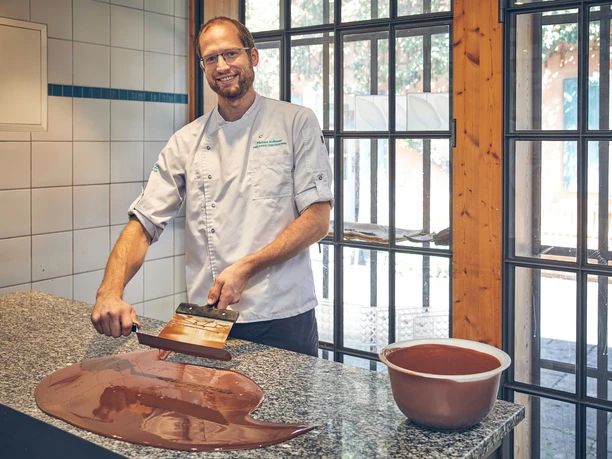 Schokoladenmanufaktur Barbara Krönner Mann in weißem Kochhemd temperiert Schokolade auf einer Arbeitsplatte in heller Küche.