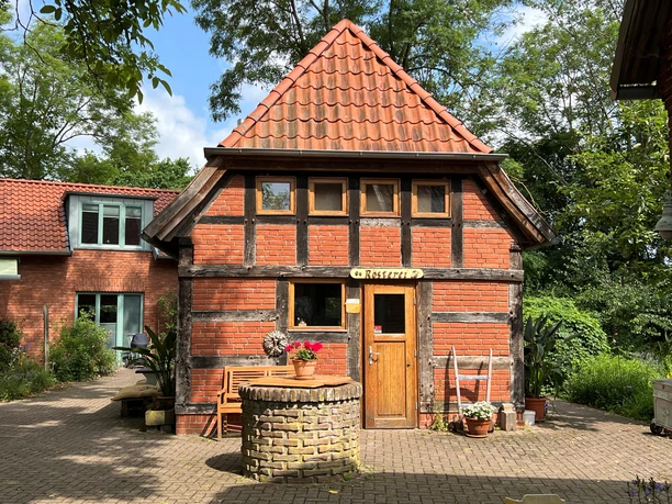 A traditional half-timbered house with a red tiled roof, surrounded by green plants and trees.