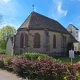 Romanische, gotisch erweiterte Saalkirche, umgeben von Rasen und Hecken