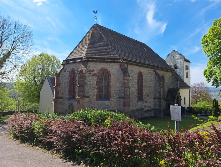 Romanische, gotisch erweiterte Saalkirche, umgeben von Rasen und Hecken
