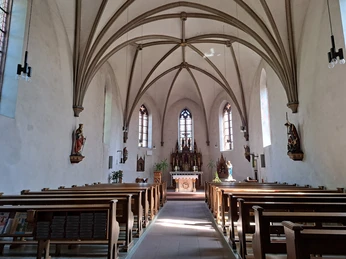 Innenansicht mit gewölbter Decke, Hochaltar und Kirchenbänken.