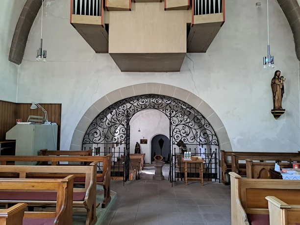 Im vorderen Bereich Kirchenbänke, schmiedeeiserner Durchgang, dahinter ein Taufbecken